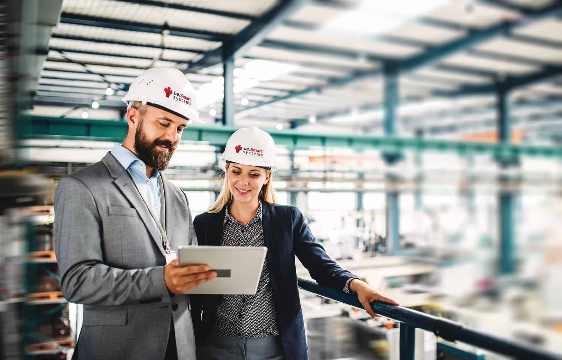 Two engineers looking at wiring schematics inside a large factory.