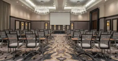 Hotel ball room turned into a conference room with stage, seating, and large projection screen.