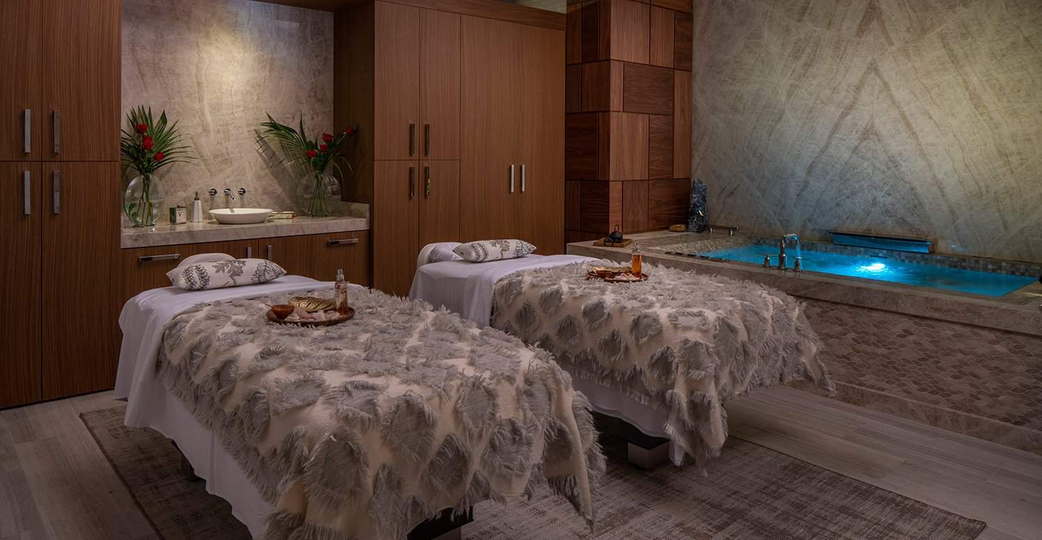 Two massage tables next to a bath tub inside a luxury spa.