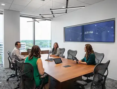Employees meeting in a small conference room with a large video display on one wall