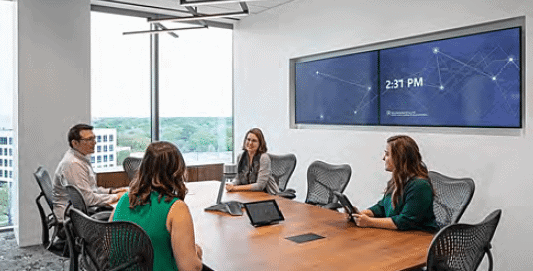 Employees meeting in a small conference room with a large video display on one wall
