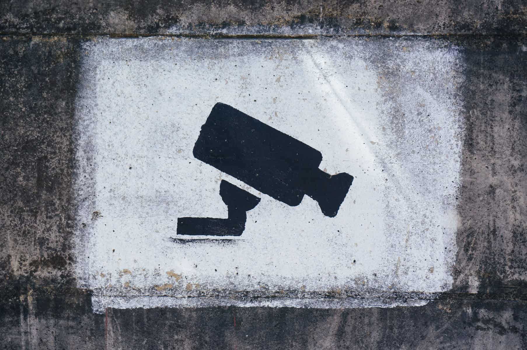 A black and white painting of a camera indicating to visitors that they are under video surveillance.